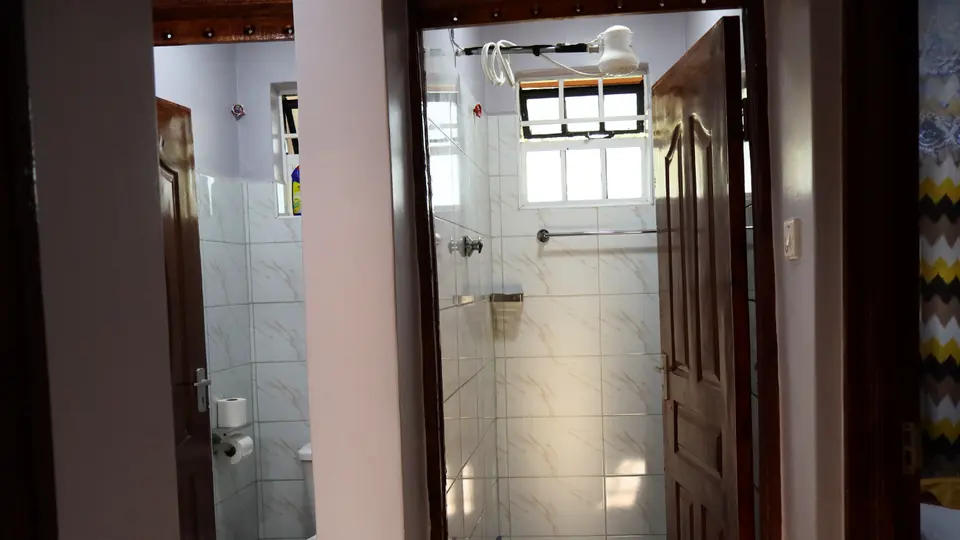 Tiled bathroom with a shower and window, next to a separate toilet