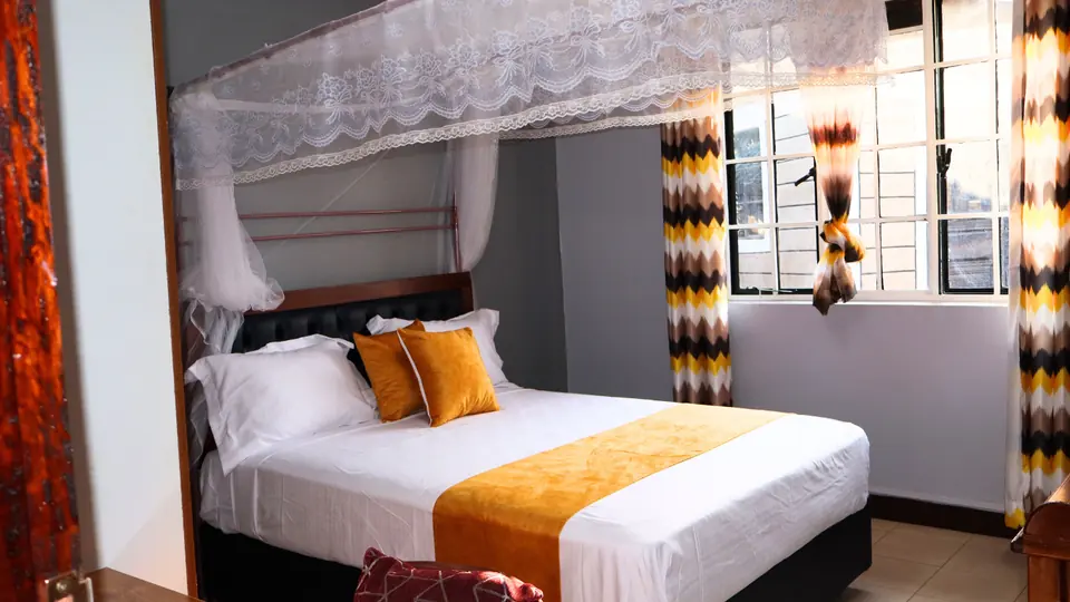 Double bed with white linen and a gold runner under a mosquito net canopy, beside a window