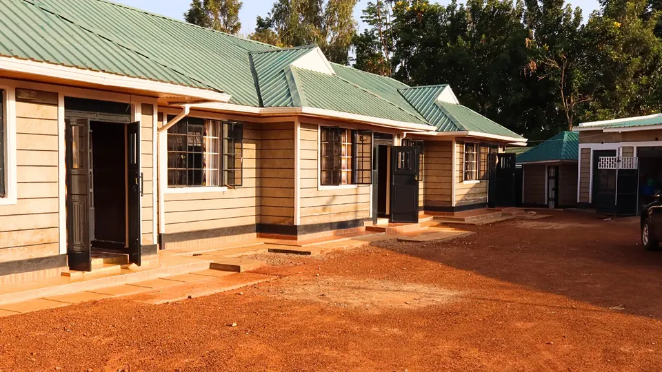 The bungalows across the compound yard under green roofs, front doors open