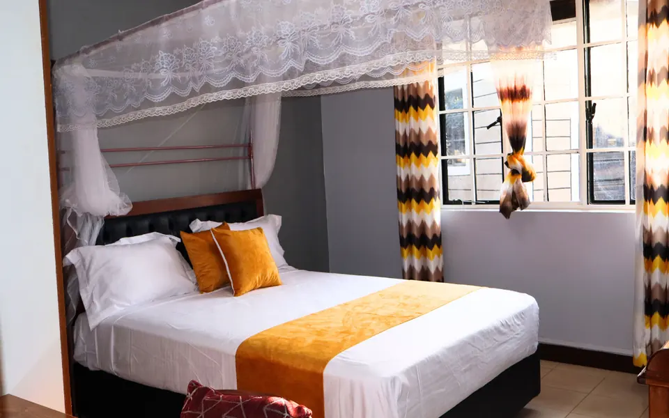 Double bed with white linen and a gold runner under a mosquito net canopy