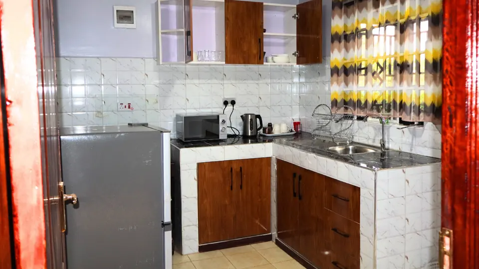 Kitchen with a fridge, microwave, kettle and tiled counter under wall cupboards